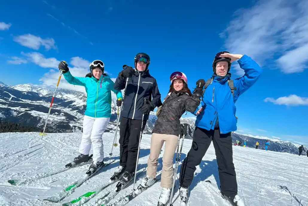 4 zufriedene IT-Mitarbeiter stehen auf Skiern in einem Bergpanorama und haben eine gute Zeit